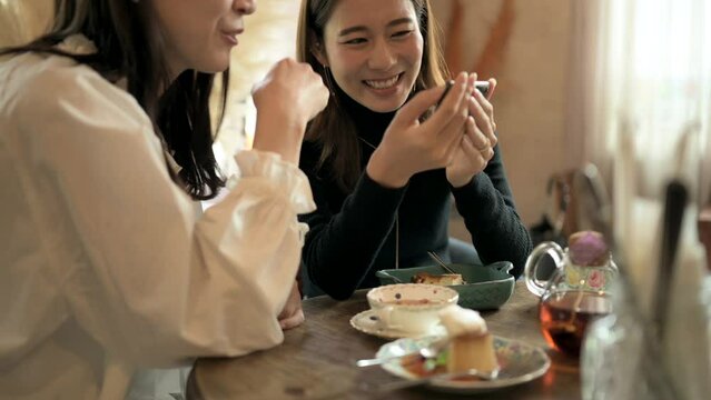カフェでスマートフォンをみて笑い合う二人の女性客
