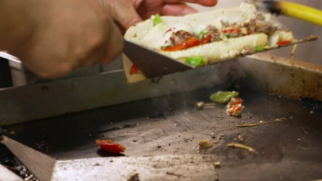 Cook uses spatula to stuff philly cheesesteak filling into steamed bun on flattop grill, close up slow motion 4K