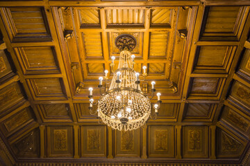 An old vintage chandelier with numerous candle-shaped lamps under the wooden ceiling of an old...