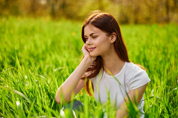 Portrait of young beautiful pensive dreamy woman lying on grass at summer green park .