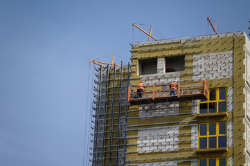 Workers sheathe the outer walls of a brick house with insulation. Insulation of the facade of the building. The concept of exterior decoration, moisture protection, sound insulation, energy saving.