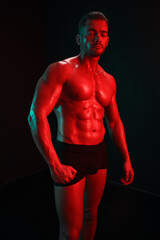 Fashion portrait of an athletic trim attractive man. Manly naked torso in his underpants. Colored flash of studio neon light.