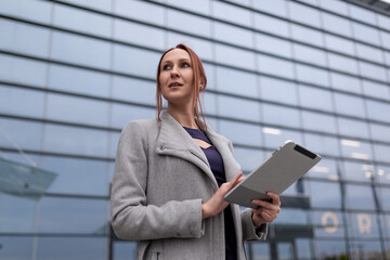 young woman designer with a ponytail hairstyle holds a tablet on the background of a large glass building