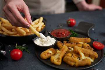 Woman dips french fries into dip sauce with Cheese fried mozzarella sticks on a table
