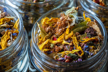 Dry flower and herbal tea leaves in a glass jar on wooden background. Herbal collection of chamomile, cornflower, mint, sea buckthorn, lemongrass, wild rose, dried citrus fruits and apple