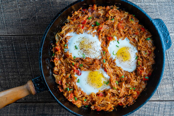 Stewed cabbage with vegetables and fried eggs in a frying pan on a wooden background, closeup, top view. Food background. Healthy food