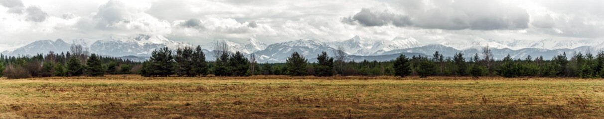 Panoramic view on Tatra Mountains, Poland seen from further. Snow-covered peaks of the rocky mountains and cloudy sky in the time of early spring. Natural background.