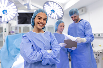 Close-up of a surgeon woman looking at camera with colleagues performing in background in operation room. The concept of medicine - obrazy, fototapety, plakaty