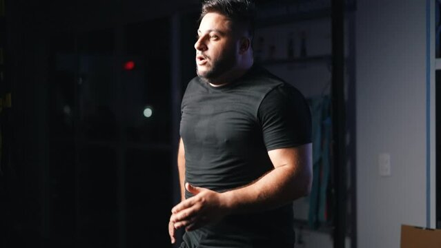 Strong man running in place as a cardio exercise for daily workout in a dark gym training hard for competition in slow motion