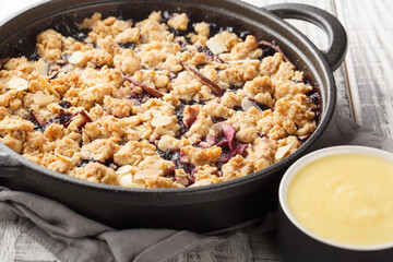 Swedish Smulpaj Crumble pie with apples and blueberries served with homemade vanilla sauce closeup on the wooden table. Horizontal