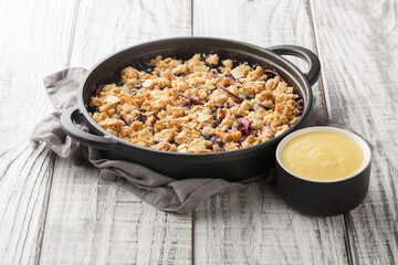 Smulpaj summer berry fruit pie baked with apples and blueberries served with vanilla sauce close-up in a pan on the table. Horizontal