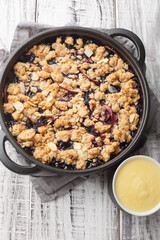 Delicious summer berry fruit pie baked with apples and blueberries served with vanilla sauce close-up on the table. Vertical top view from above