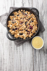 Swedish pie Smulpaj baked with apples and blueberries close-up in a pan on the table. Vertical top view from above