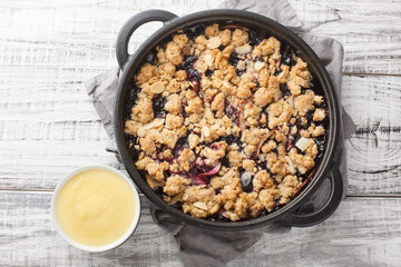 Berry fruit crumble baked with apples and blueberries served with vanilla sauce close-up in a pan...