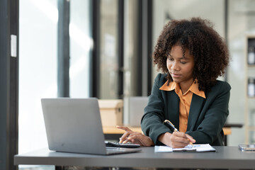 African american businesswoman working with laptop looking at financial information Successful business results in modern office with happy note taking in folder.