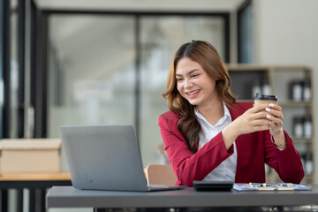 Smiling asian businesswoman holding cup of coffee relaxing after working on finance business and marketing at modern office.