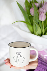 A woman's hand holds a cup filled with coffee. Behind a bouquet of tulips. 