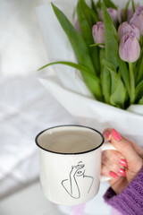 A woman's hand holds a cup filled with coffee. Behind a bouquet of tulips. 