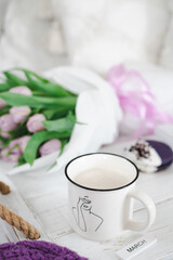 A cup filled with coffee. Behind a bouquet of tulips. The inscription March on the plate