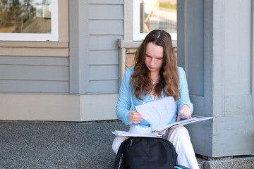 teenager girl does homework on porch of house she writes with pencil in large notebook notebook in...