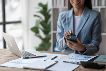 Asian businesswoman, investor, insurance salesman pointing at mobile phone to search and view financial details. Customer database in the real estate project business at the desk in the office.