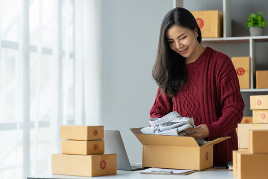 small business startup images SME business owner, female entrepreneur packing shirts , Shirts for work to prepare packs sent to customers via express delivery companies, SME business concepts online.