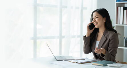 copy space, panorama ,banner , Happy young asian woman talking on the mobile phone and smiling while sitting at her working place in office.