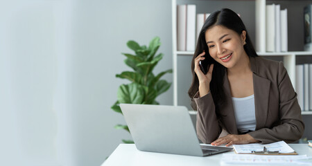 copy space, panorama ,banner , Happy young asian woman talking on the mobile phone and smiling while sitting at her working place in office.