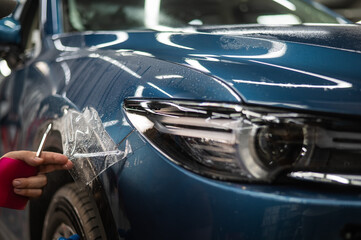 Fototapeta premium The master in the car service applies an armor film to the car. 