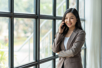 Asian business woman financially successful entrepreneur professional company executive Wearing a suit standing and talking on a mobile phone in business information in the office.