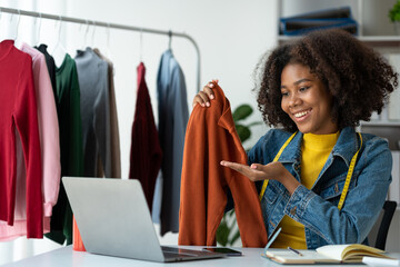 American business woman african, tailor A small business owner is selling clothes online, an online ordering app through a colorful laptop computer to customers at his home office.