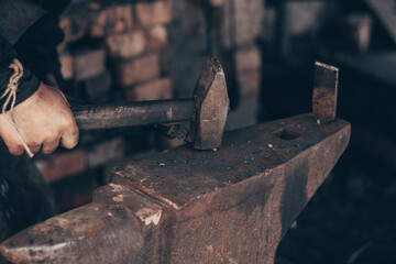 Blacksmith working metal with hammer and pincers on anvil in forge. Farrier strike iron in workshop. Metalworking, manufacturing equipment and tools. Traditional technic of making hardware.