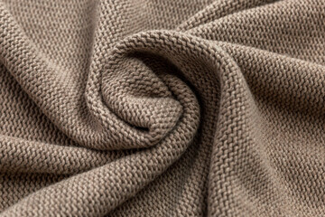 The surface of a brown knitted fabric laid in waves. Needlework and hobbies. Close-up.