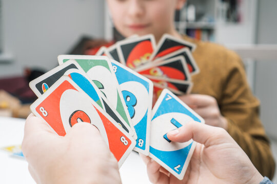 Belarus, Minsk, 08.01.2023. Boys play UNO. Hands of children hold paper colorful cards with numbers in fan closeup.