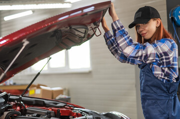 Fototapeta premium Woman auto mechanic opens the hood of a car in a car service. 