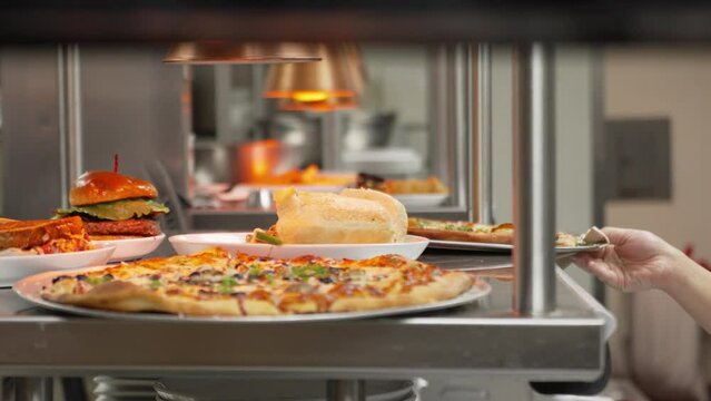 Server pulls platter from classic American restaurant kitchen pass window filled with various types of food, pizza, burgers, sandwiches, slider slow motion 4K