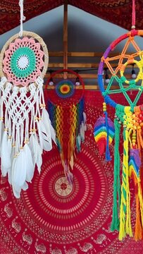 vertical footage of colorful dream catcher hangs and swirls in the wind with a red tribal cloth hanging at background.