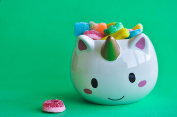 cute vase in the form of a unicorn with gummy bears on a colored background