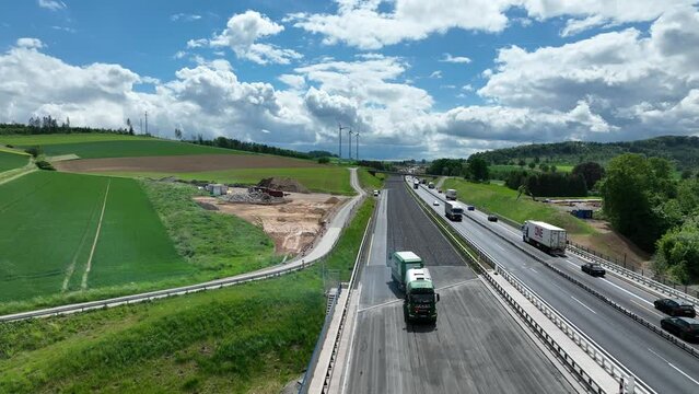 Droneshot of german highway construction site. Large construction vehicle laying out fresh tarmac. Ongoing traffic next to it, Sunny weather with green trees in the background.