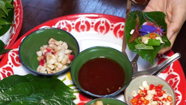 Wooden spoon put sauce and pouring on many kind of vegetable in betel leaf and pack it to make a royal leaf wrap appetizer or "Miang kham", one famous thailand traditional food menu.