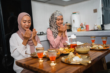 two woman pray before meals when breaking the fast together at home