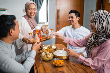 muslim woman serving drink for her friend and family at home having dinner together