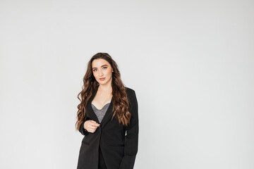 young businesswoman with long curly hair in a black suit stands on a white background