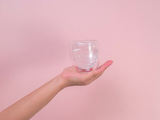 Female hand holding glass of water isolated on pink background.
