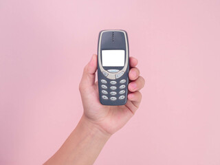 Close up hand holding mobile phone Nokia 3310 isolated on pink background. Female hand holding old...