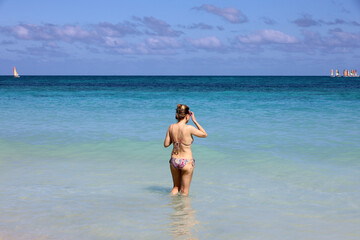 Woman in bikini standing blue sea water and looking to sailboats on horizon. Beach vacation on Caribbean islands