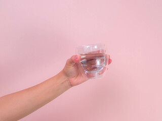 Female hand holding glass of water isolated on pink background.