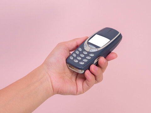 Close up hand holding mobile phone Nokia 3310 isolated on pink background. Female hand holding old used phone Nokia 3310.