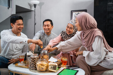 Muslim friends chatting while taking snacks from a jar during a visit to celebrate Eid at a friend's house
