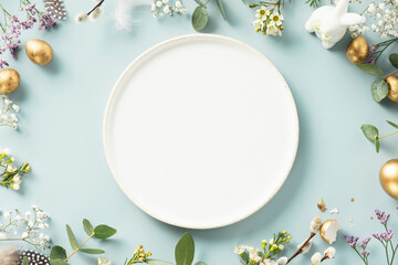 Happy Easter concept with white plate, golden easter eggs, feathers and spring flowers. Easter background with copy space. Flat lay